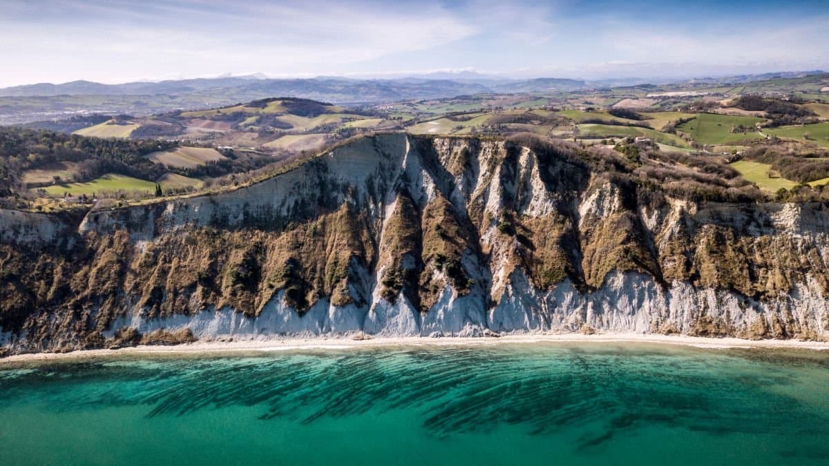 Veduta aerea della costa vicino Pesaro: alte falesie bianche a picco sul mare turchese, con le colline coltivate alle spalle