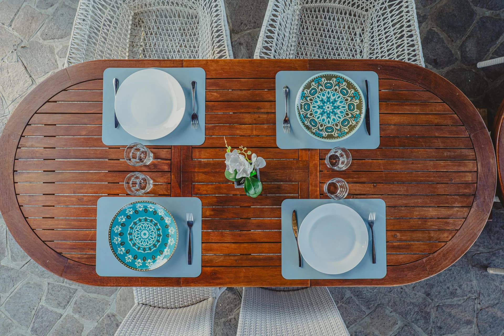 Veduta dall'alto di un tavolo ovale in legno apparecchiato con piatti decorati blu, bicchieri e un'orchidea al centro
